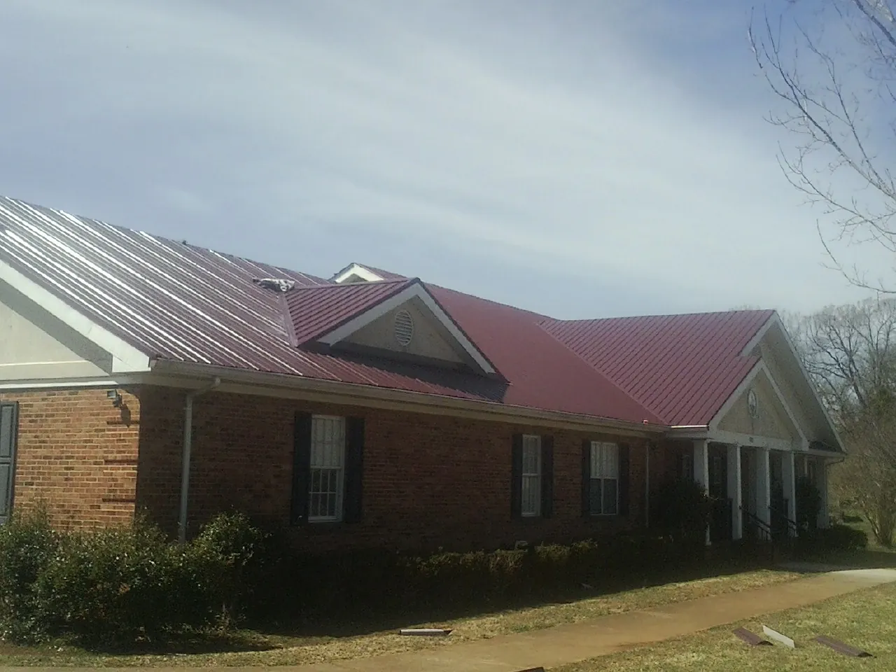 Red metal roof with gabled entries on a long brick building, from a Hail Damage Roof Repair job in Centertown