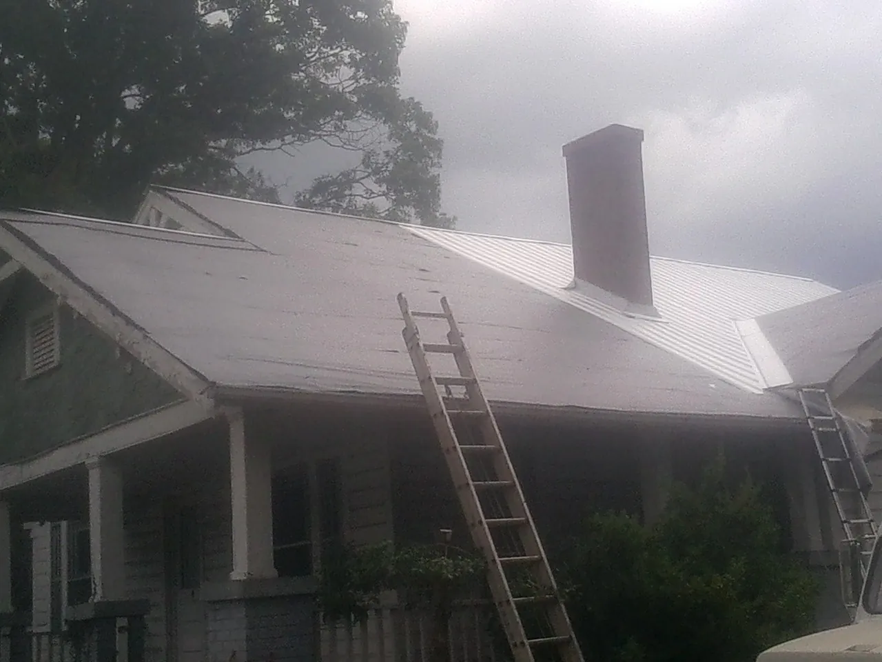 Ladders against a metal roof on an older home with a brick chimney in Centertown