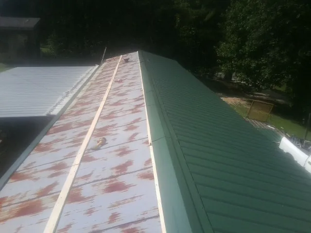 Old rusted panels beside newly installed green metal roofing — Wind Damage Roof Repair by Roofing Brothers in Centertown