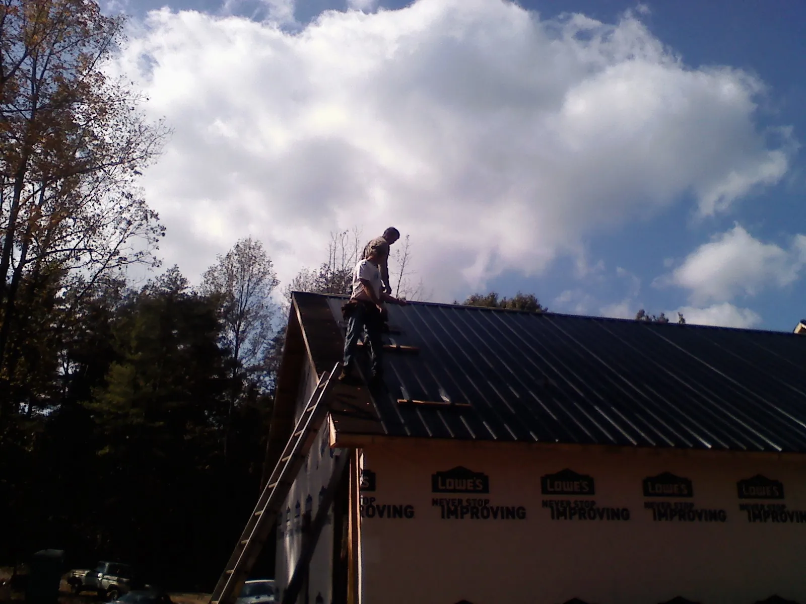 Roofer fastening dark metal panels high against a cloudy sky, from a Roof Inspection job in Centertown