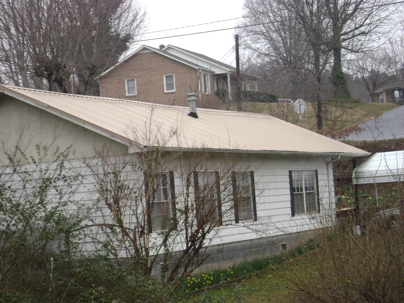 Tan metal roof on a white sided house set into a hillside — Commercial Roofing by Roofing Brothers in Centertown